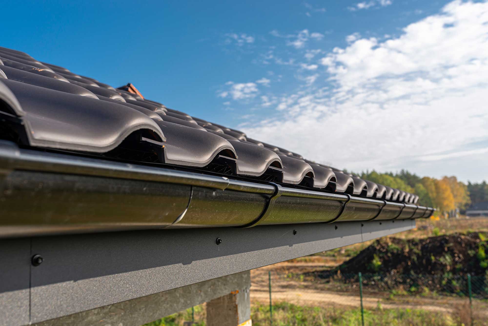 A metal black gutter on a roof covered with ceramic tiles