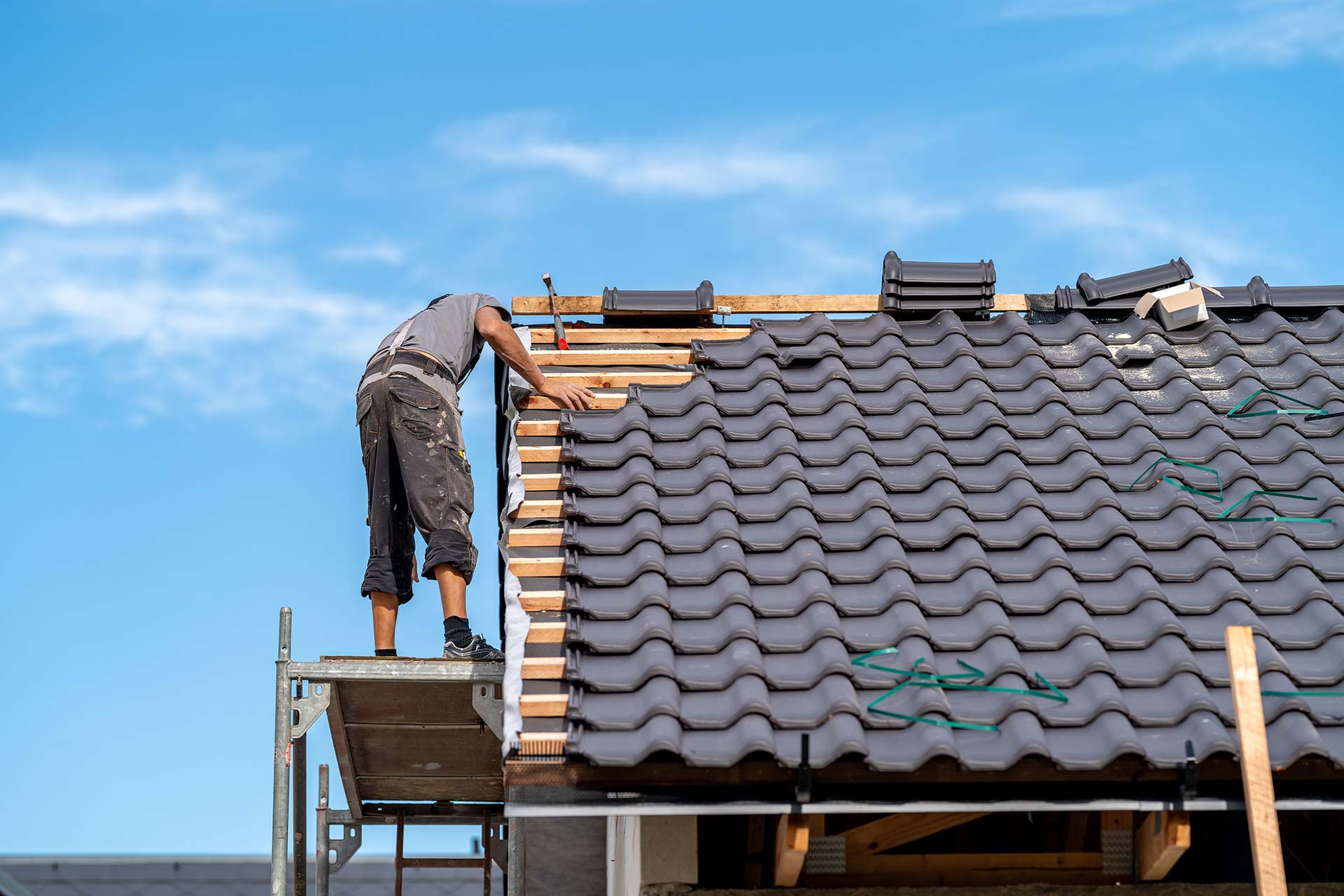A man is working on a tiled roof, carefully inspecting and repairing the roofing materials.