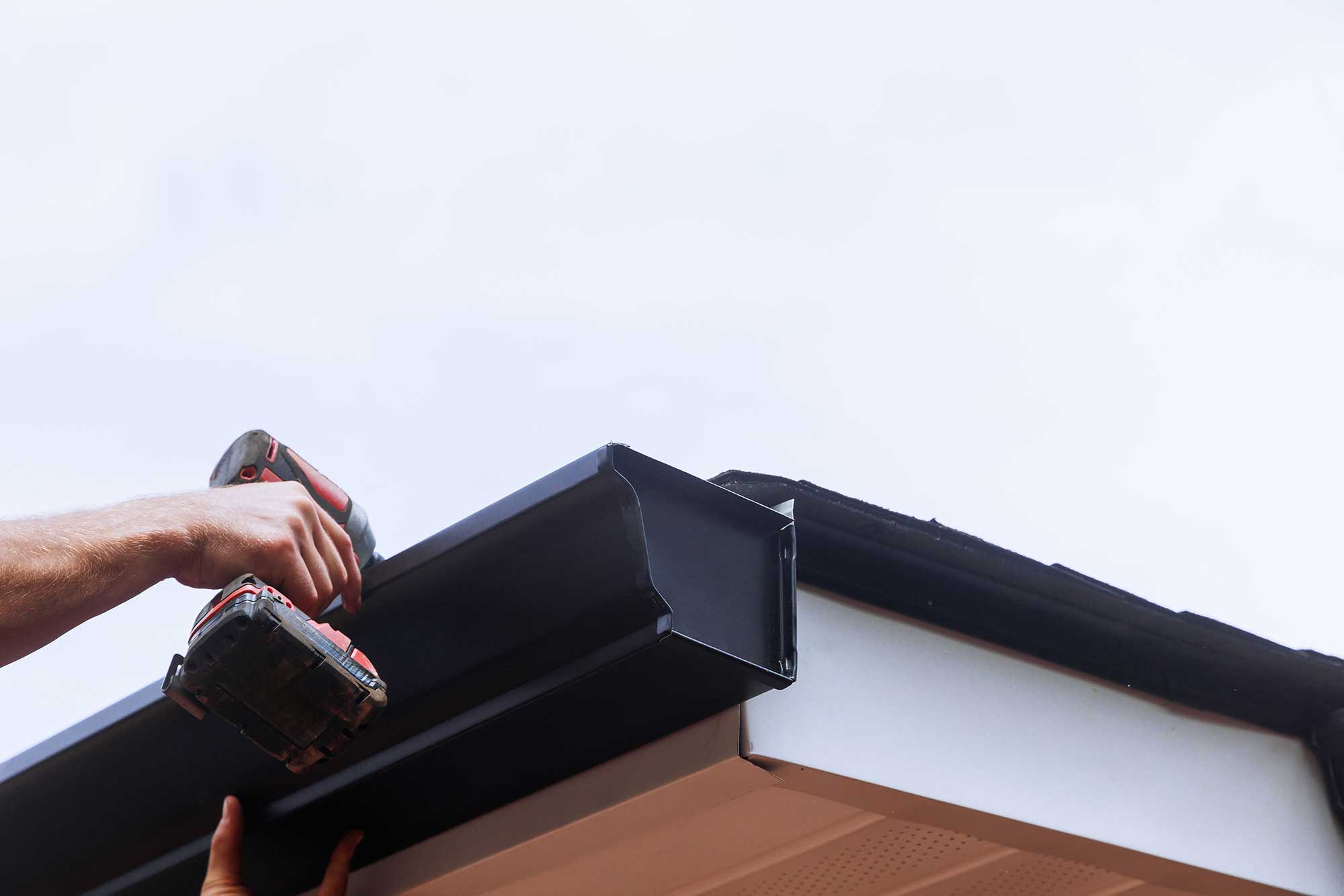Worker installing rain gutter on roof